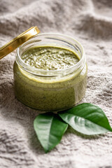 Natural green scrub with sugar in a glass jar on the background of cloth and leaves. Concept of organic cosmetics and skin care