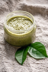 Natural green scrub with sugar in a glass jar on the background of cloth and leaves. Concept of organic cosmetics and skin care