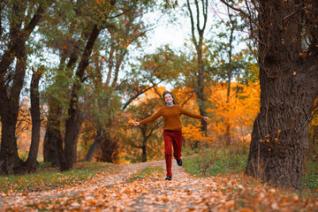 a young teenage girl runs through the autumn forest along a dirt road and enjoys the beautiful nature and bright yellow leaves