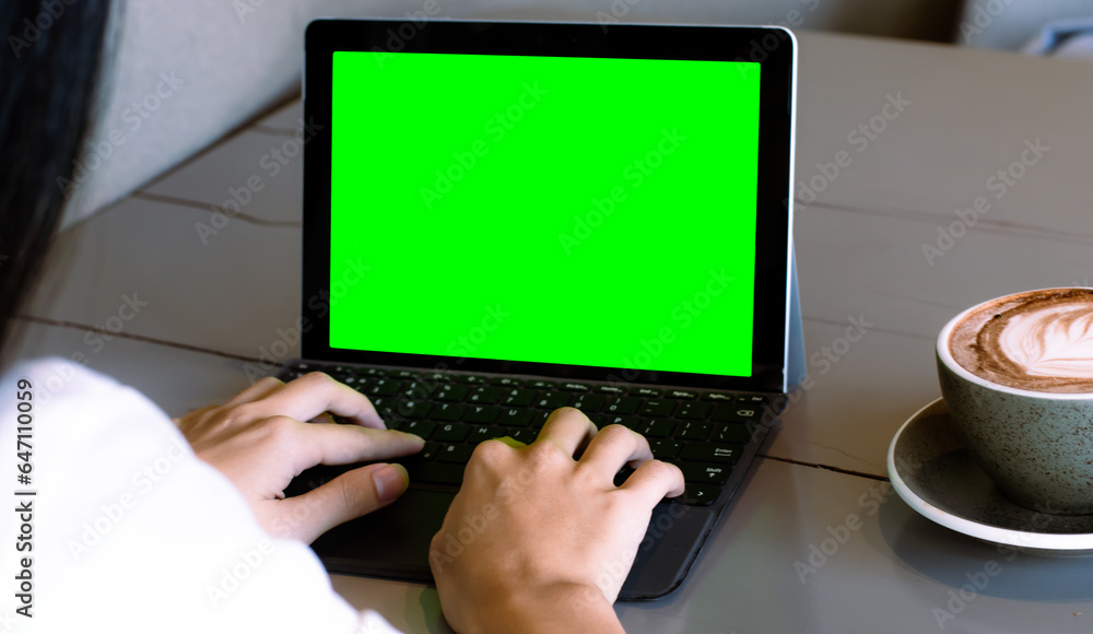 Poster close up of freelencer using laptop computer with mock up green screen chroma key display in cafe.