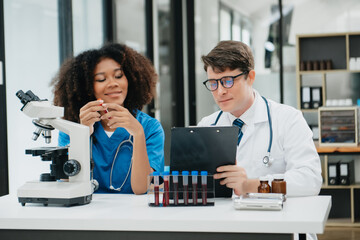 Focused mature male doctor and African female nurse look at tablet and laptop screen discuss anamnesis together. Concentrated diverse medical professionals