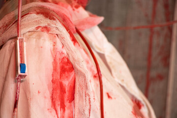 A bloody white medical gown of a nurse, covered in blood and a drip, hangs on the gown, a doctor's...