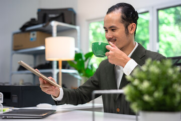 The manager of an Asian man sipping coffee on his desk in a radiant manner.
