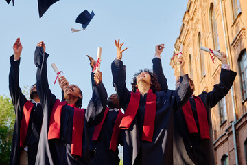 Group of students in gowns tossing their hats up while standing outdoors near the university