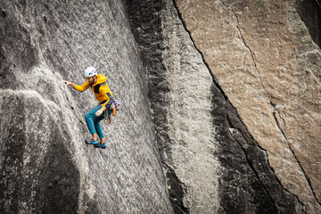 Person climbing in high mountains with yellow jacket rope and helmet in nature, confidence and...