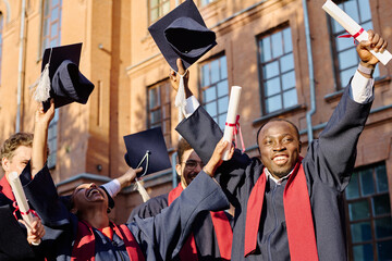 Group of excited multiethnic students in graduation gowns getting diplomas