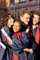 Vertical image of happy students embracing each other, they graduating from university - obrazy, fototapety, plakaty