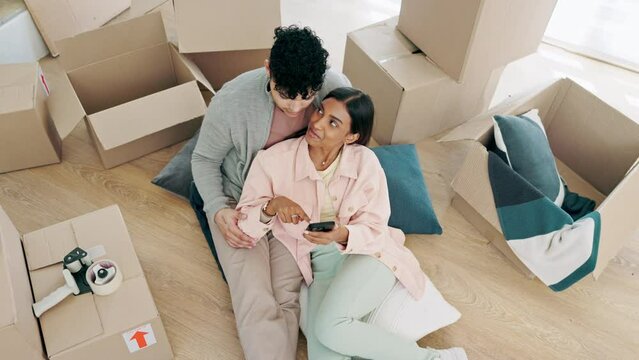 Happy couple, real estate and phone in relax, planning or moving in new home together above in living room. Top view of man and woman with boxes in property investment, online or house renovation