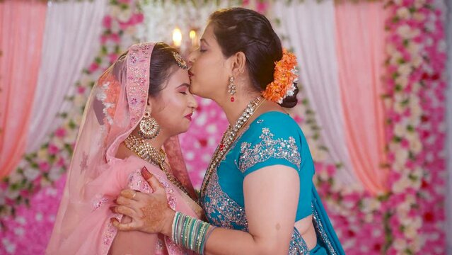 happy loving mother kissing daughters forehead by hugging her bridal daughter during wedding on stage - concept of Emotional Moment, parental blessings and traditional culture