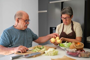 Mature Spanish couple cooking cocido madrileño, typical Spanish dish, in a modern kitchen.