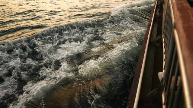 Slow motion close up of bow cutting through the water waves at sunset. View from the side of the vessel. 
