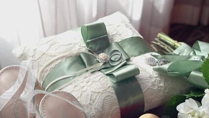 Two white gold wedding rings on a pillow with green ribbon, on a wooden table. Wedding details