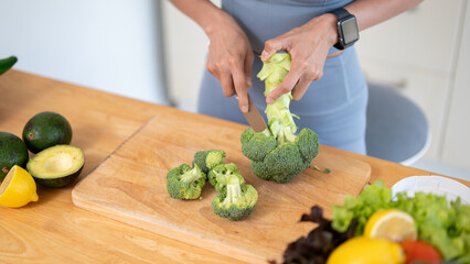 A fit woman in gym clothes is cutting broccoli on a chopping board, preparing her healthy breakfast.