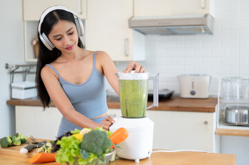 Obraz na płótnie Canvas A fit and beautiful Asian woman in sportswear is making her healthy smoothie in the kitchen.