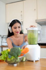 A gorgeous Asian woman in sportswear is making her healthy green detox smoothie in the kitchen.