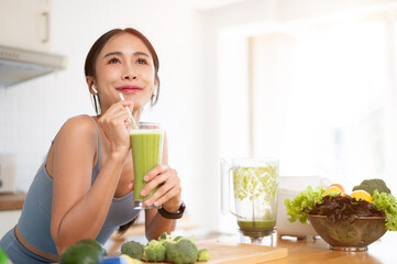 A beautiful Asian woman is enjoying her healthy green smoothie in the kitchen after her workout.