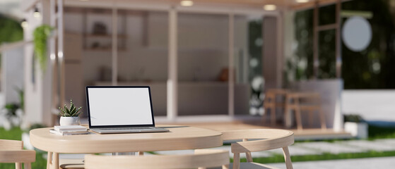 A laptop mockup on a table in a minimalist coffee shop or restaurant's outdoor seating space.