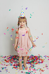 Happy kid girl standing with confetti against white studio wall background. Full length of girl child with confetti rain, birthday party concept