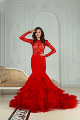 Elegant perfect model woman in red evening gown. Nice sensual lady with perfect makeup and hairstyle posing in luxurious interior