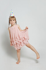 Happy attractive funny child girl in birthday party hat posing on white background