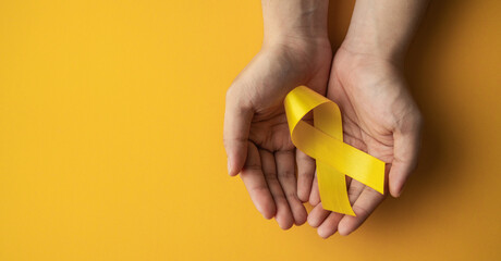 yellow ribbon on the hand of a cancer sick person, world cancer day, healthcare and medicine backdrop, suicide prevention, children health care.