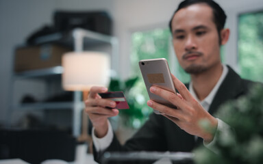 Asian businessman smiling and happy doing online shopping outside office building, man using mobile phone, holding bank credit card