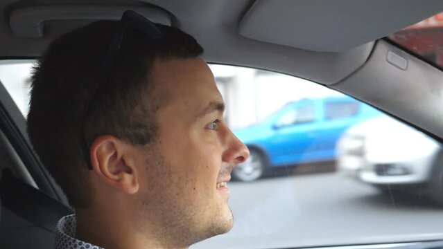 Profile of happy businessman in shirt driving automobile and talking. Male driver riding a car at city and speaking. Young man commuting to work. Side view from the salon. Close up Slow motion