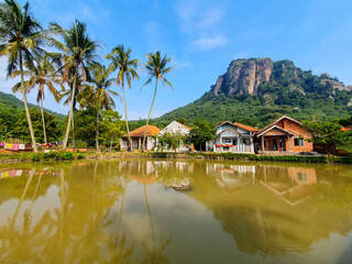 Fototapeta premium House in the countryside near the river with a mountain on background under the blue sky. Beautiful view of the village