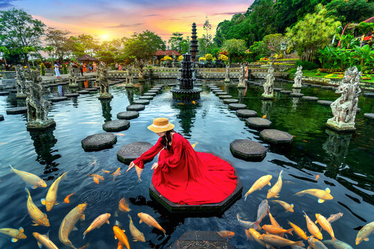 Woman feeding colorful fish in pond at Tirta Gangga Water Palace in Bali, Indonesia.