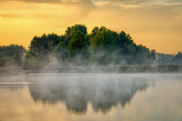 Fototapeta na wymiar Scenic view of a country lake landscape with trees reflected in the water and fog. Morning of the beginning of autumn.