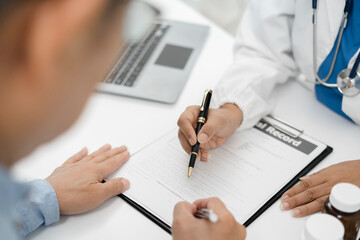 Female doctor consulting senior old patient filling form at consultation, talking to senior old patient filling signing medical paper at appointment visit in clinic.
