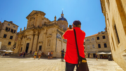 a tourist takes pictures of a church in the old town, while other tourists stroll down the street...