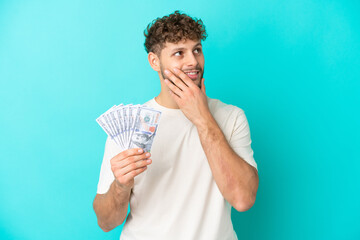 Young caucasian man taking a lot of money isolated on blue background looking up while smiling