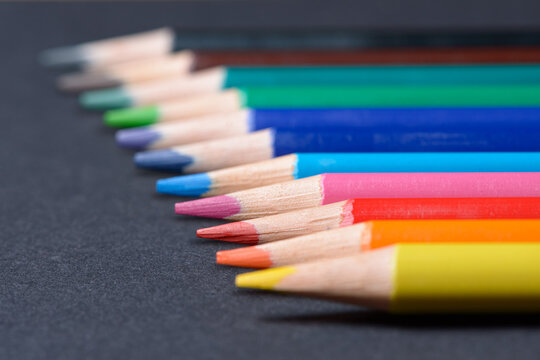 Collection set of colored pencils crayons orderly aligned in a row, art or drawing equipment on dark background.