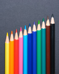 Collection set of colored pencils crayons orderly aligned in a diagonal row, art or drawing equipment on dark background.