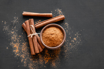 Cinnamon sticks and cinnamon powder on dark rustic background, healthy spice, (Cinnamomum)