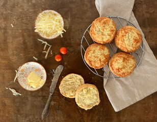 Overhead view of spelt flour cheese scones on an old wooden table with cheese, butter, an old knife...