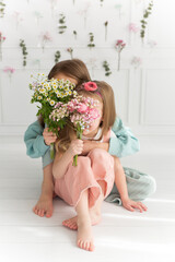 Two sisters hug and cover their faces with bouquets of flowers