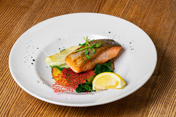 Fried salmon steak with potatoes and vegetables on wooden table