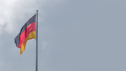 Naklejka premium National black red yellow flag of Germany and at dramatic sky solid background with copy space. Concept of nationality, citizenship and economical crisis and recession