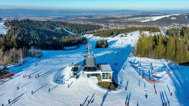 Ski slope, chairlift, skiers and snowboarders in Bialka Tatrzanska ski resort in Poland on Jankulakowski Wierch Mountain in winter. Aerial 4K panning video in sunset light