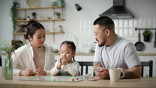 Asian Family Playing Board Game Together. Happy young family with one kid plays board card game with dies sitting at home.