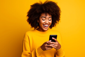 Woman laughs and types on smartphone in studio, reading funny social media posts and mobile news on yellow background. happy african model