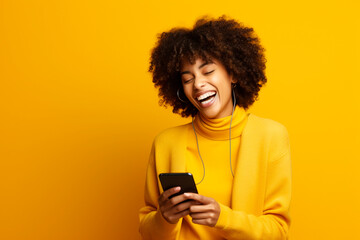 Woman laughs and types on smartphone in studio, reading funny social media posts and mobile news on yellow background. happy african model - obrazy, fototapety, plakaty