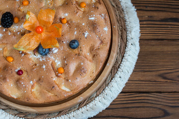 A cooked apple pie on a wooden background decorated with a physalis flower, blackberries and cranberries. Apple charlotte