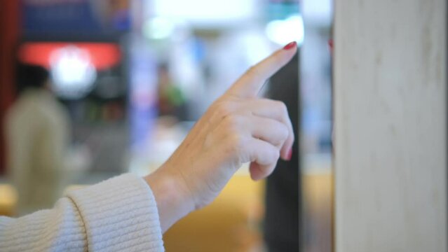 Girl using touch terminal makes a quick order through the self-service. Woman choosing dessert via self-service machine at fast food restaurant. Person swipes the screen making an order.