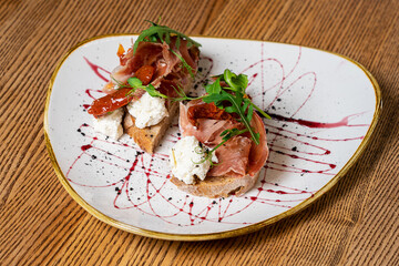 Bruschetta with prosciutto, hard cheese, herbs and spices on a wooden board. Tasty breakfast.