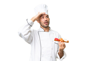 Young caucasian chef holding a sushi over isolated background doing surprise gesture while looking to the side
