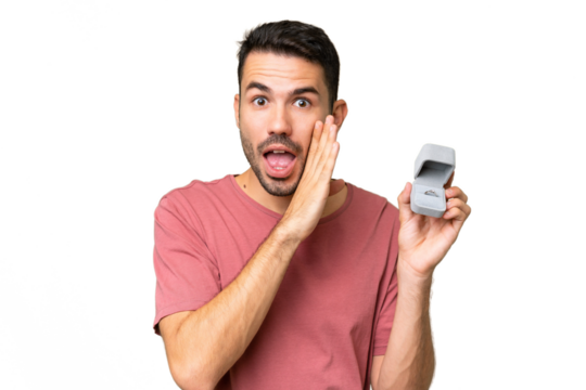 Young handsome caucasian man holding a engagement ring over isolated background whispering something - Powered by Adobe