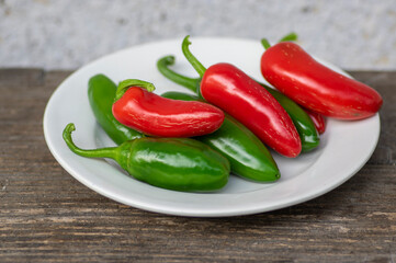 Capsicum annuum Jalapeno chilli hot peppers, group of green and red fruits on wooden brown table on white plate